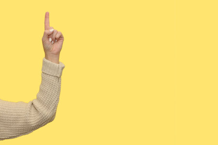 A woman's hand in a jumper holds a thumbs up. Gesticulation and pointing. On a yellow background.の写真素材