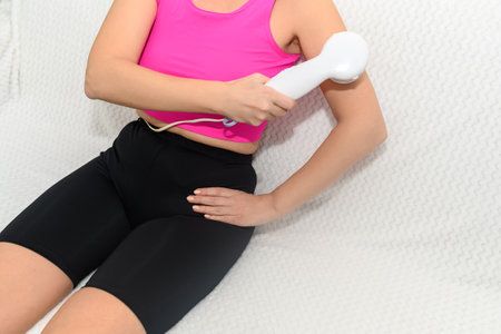 A woman in sportswear makes a cosmetic massage at home on the couch.の写真素材