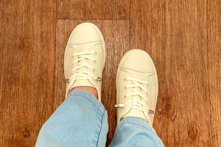 Women's legs in blue jeans and white sports shoes. With white laces. They stand on the floor.の写真素材