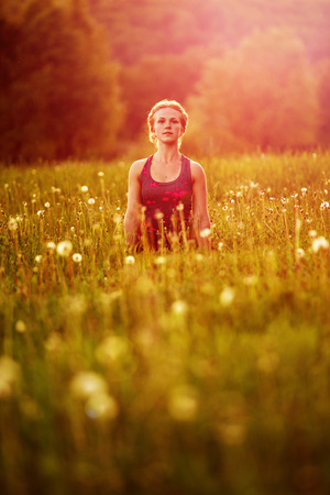 Young woman in a relaxing yoga pose at the evening meadow vertical shotの写真素材