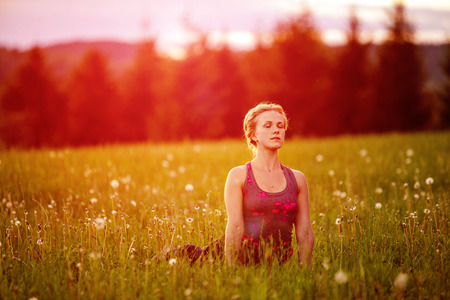 Young woman in a relaxing yoga pose at the evening meadowの写真素材
