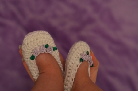baby legs in knitting white slippers with purple roses on the armの写真素材