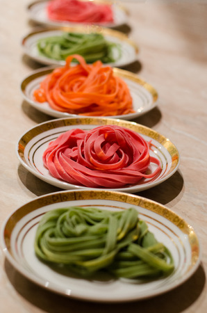 Red, Green and Orange Spaghetti on White Dishes with Gold Bandeletの写真素材
