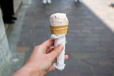 Close up image of girl hand holding fresh waffle cone with vanilla and raspberry ice cream on the...