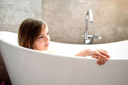 Relaxed young girl model wears towel wrapped on head, feels refreshed after taking shower, has healthy clean soft skin, poses in cozy bathroom. Girl, beauty and hygiene concept. High quality photoの写真素材