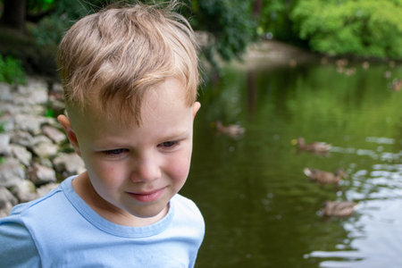 A little boy wearing a blue shirt is playing on a pond with ducks. Vacation resort. High quality...