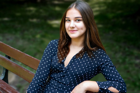 Emotional girl teenager with long hair hairstyle braids in a green shirt sits on a bench in the park. High quality photoの写真素材