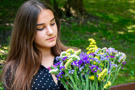 Emotional girl teenager with long hair hairstyle braids in a green shirt sits on a bench in the park. High quality photo. High quality photoの写真素材