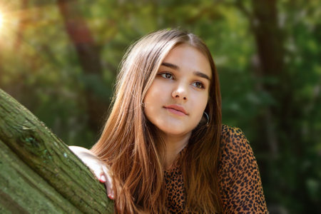 Emotional girl teenager with long hair hairstyle braids in a green shirt sits on a bench in the park. High quality photo. High quality photoの写真素材
