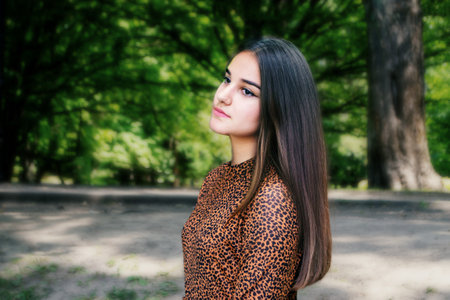 Emotional girl teenager with long hair hairstyle braids in a green shirt sits on a bench in the park. High quality photo. High quality photoの写真素材