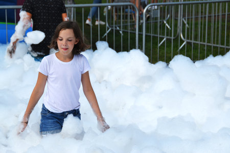 happy girl with foam on her head, in wet clothes at a foam party, in wet clothes at a foam party or holiday on a sunny hot summer day. High quality photoの写真素材