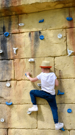 The boy is engaged in rock climbing. Climbing harness safety sports equipment. Rope amusement city park, obstacle course. Kids children's attraction center. High quality photoの写真素材