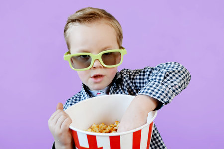 Little cute fun kid baby boy 3-4 years old in red t-shirt holding bucket for popcorn, eating fast food isolated on yellow background. . High quality photoの写真素材