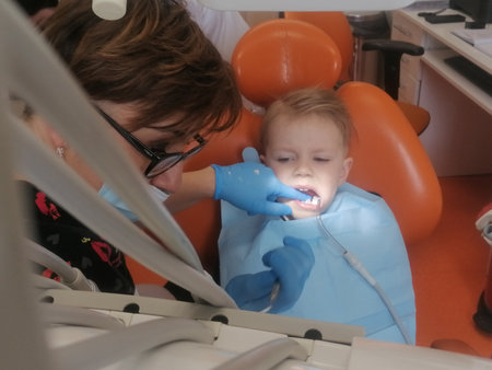 Female dentist examines the teeth of the patient cheerful child with curly red hair. Moloi boy smiling in dentist's chair. child mouth wide open in the dentist's chair. High quality photoの写真素材
