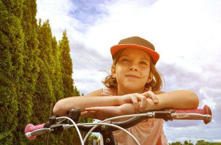 Young girl cyclist enjoy the beautiful sunrise on summer forest trail. Close-up portrait of a happy little girl in a helmet on a bicycle. High quality photoの写真素材