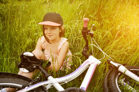 Young girl cyclist enjoy the beautiful sunrise on summer forest trail. Close-up portrait of a happy little girl in a helmet on a bicycle. High quality photoの写真素材