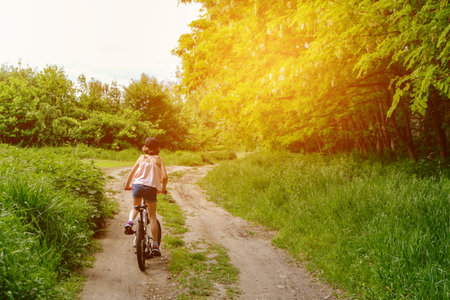 Young girl cyclist enjoy the beautiful sunrise on summer forest trail. Close-up portrait of a happy little girl in a helmet on a bicycle. High quality photoの写真素材