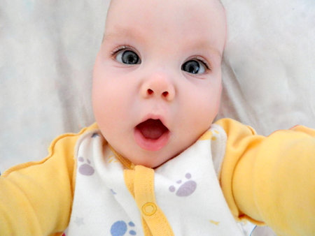 Adorable baby girl in white sunny bedroom in winter morning. Newborn child relaxing in bed. Family morning at home. Newborn kid during tummy time smiling happily at home. High quality photoの写真素材