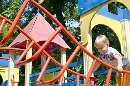A child climbs up an alpine grid in a park on a playground on a hot summer day. children's...