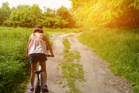 Young girl cyclist enjoy the beautiful sunrise on summer forest trail. Close-up portrait of a happy little girl in a helmet on a bicycle. High quality photoの写真素材