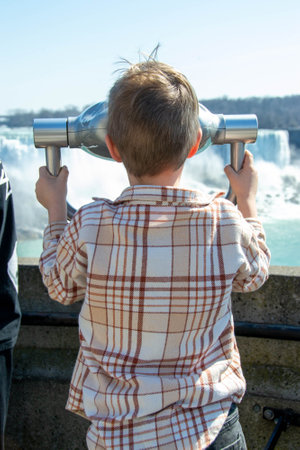 Boy looking through the viewing binoculars on the balcony across the American and Bridal Veil Falls...