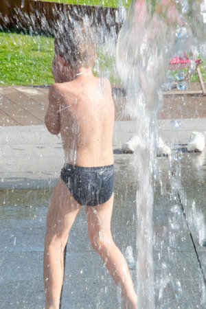 A boy plays with water in a park fountain. Summer is here. Little boy plays in the square between the water jets in the dry fountain on sunny summer day. Active summer leisure for kids in the city. High quality photoの写真素材