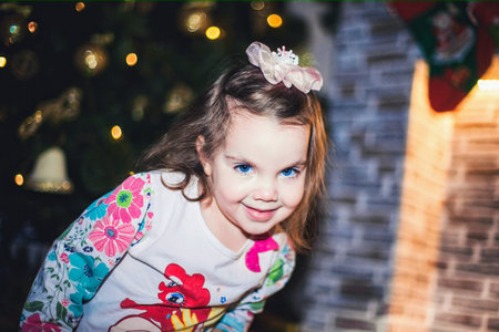 A happy toddler is smiling in front of a Christmas tree and fireplace, enjoying the festive event....