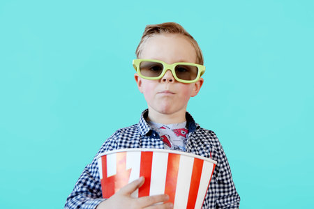 Little cute fun kid baby boy 3-4 years old in red t-shirt holding bucket for popcorn, eating fast food isolated on yellow background. . High quality photoの写真素材