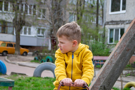 A boy in a yellow jacket is sitting on a tree stump. A boy plays with a toy car in the sand. A person is using a yellow plastic shovel to dig sand. High quality photoの写真素材