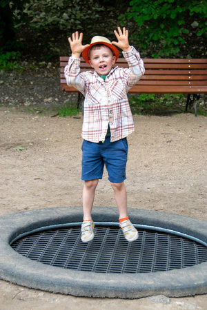 Happy kid plays outdoors in garden jumping high in the sky on trampoline. Active teenager boy having...