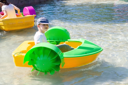 Kid playing rowing water paddle boat. Soft focus. A little girl rides a colorful boat on a pool in a...