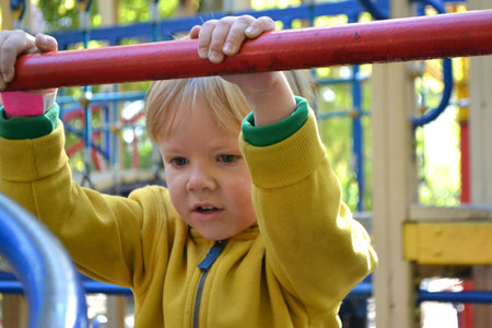 Blond haired boy has fun at playground in local park. High quality photo