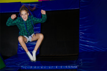 Happy active emotional preteen girl bouncing on trampoline while having fun in indoor amusement...