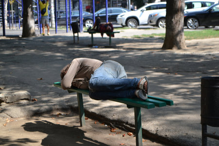 A homeless man is sleeping on a park bench or relaxing on a bench in an urban environment. Background with copy space for text. High quality photoの写真素材