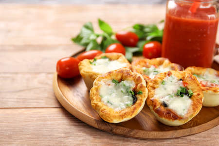 Small pizzas with mozzarella cheese, ham, olives and green onions on a wooden plate. With tomato juice in a glass jar on a natural kitchen table. Close-up.の写真素材
