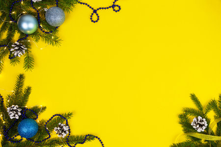 New Years festive yellow background with blue balls, spruce cones and branches and garland. Flatly. Copy space.の写真素材
