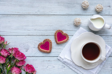 Homemade cookies in the form of hearts with pink jam with a cup of tea on wooden light blue boards with roses. The concept of Valentines Day. Flat lay.の写真素材