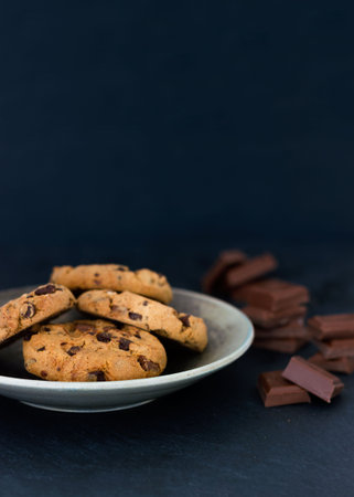 Chocolate chip cookies on a plate with chocolate pieces on a dark background