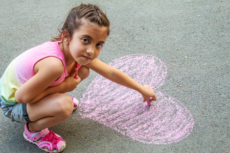 the child paints chalk on the asphalt heart. Selective focus. Draw.の写真素材