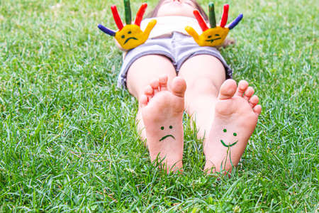 Baby feet with paint pattern are smiling and sad on the green grass. Selective focus.の写真素材