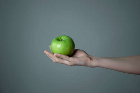 Woman`s hand holding green apple gray neutral backgroundの写真素材