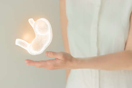 Unrecognizable female patient in white clothes, highlighted handrawn stomach in hands. Human digestive system issues concept.の写真素材