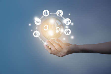 Woman`s hand holding glowing light bulb with energy resources icons. Ecological friendly and sustainable environment concept. Electricity and energy saving, energy sources.の写真素材
