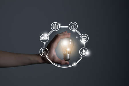 Woman`s hand holding glowing light bulb with energy resources icons. Ecological friendly and sustainable environment concept.の写真素材