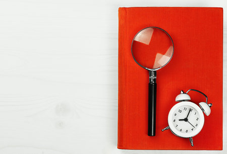 on a white wooden table, an alarm clock with a red book and a magnifying glassの写真素材