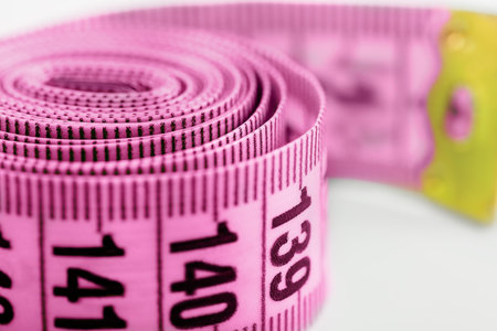 pink measuring tape, rolled up. close-up on a light background