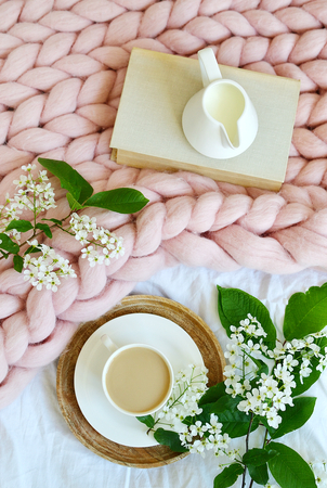 Cup with white coffee, milk, pink pastel giant blanket, bedroom, morning concept, bird cherry tree flowers, book readingの写真素材