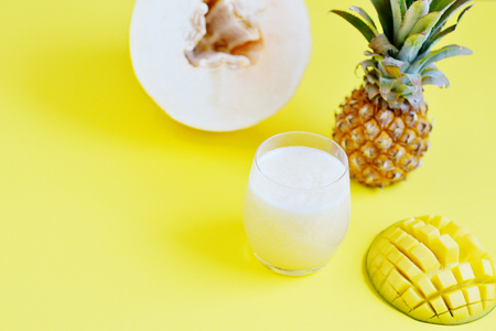 Cold fresh melon mango pineapple smoothie in glass, summer drink beverage, healthy food concept, freshness, exotic fruits, yellow background, flat layの写真素材
