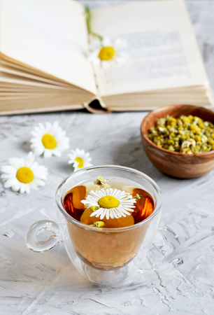 Cup of tea with chamomile flowers on gray background, book reading, free time conceptの写真素材