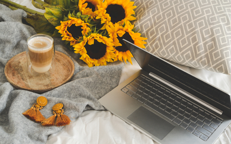 Cup with hot cappuccino, gray pastel woolen blanket, sunflowers, bedroom, morning conceptの写真素材